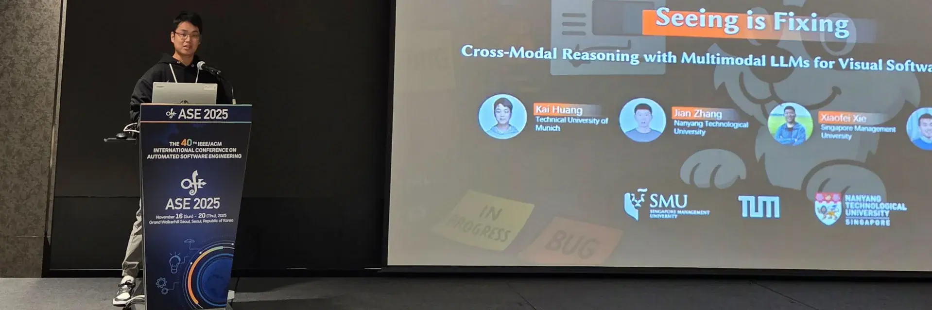 [Translate to German:] A man speaking at a conference, engaging the audience while standing next to a display screen with presentation materials.