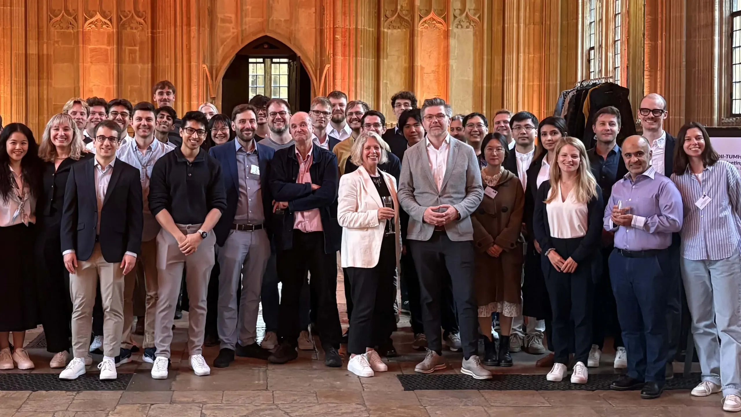 [Translate to German:] A large, diverse group of researchers has gathered for a group photo in a magnificent hall. The faces of the people look happy and relaxed.