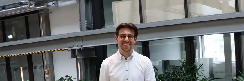 Young man in white shirt and black pants leaning against a railing in a modern building