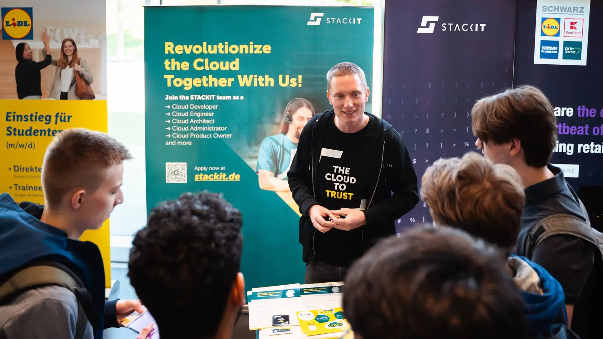 Unternehmensstand auf der Career Factory am TUM Campus Heilbronn mit Werbebannern und einem Unternehmensvertreter im Gespräch mit Studierenden.