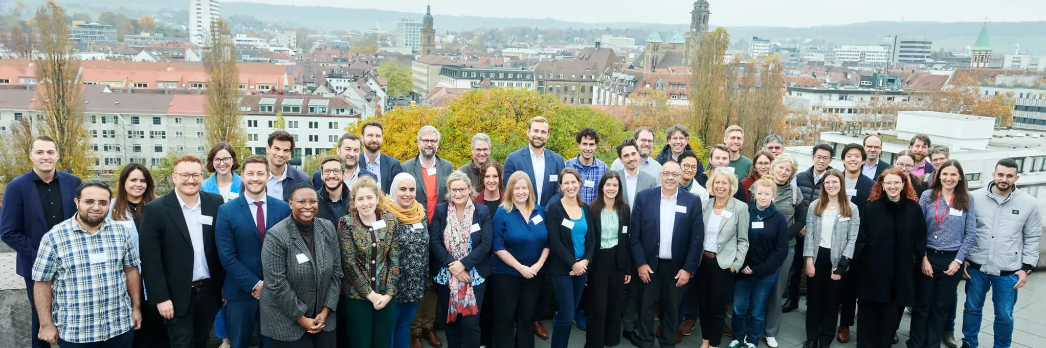 Eine diverse Gruppe von Menschen posiert zusammen auf einem Dach vor dem Heilbronner Stadtpanorama. Die Gruppe repräsentiert die Teilnehmenden des Global Technology Forum 2024.