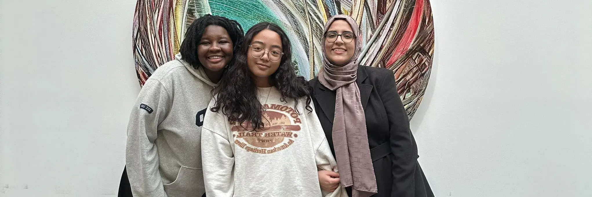 Three women pose in front of a large circular artwork.