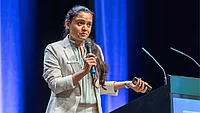 A formally dressed speaker presenting at an event