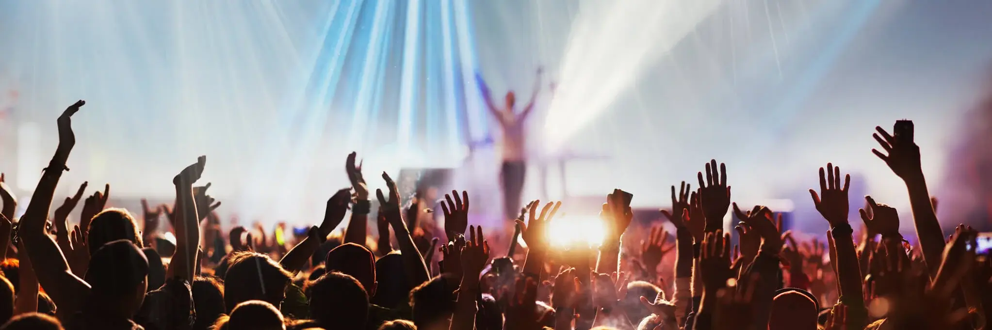 A vibrant concert scene featuring a crowd of enthusiastic attendees with their hands raised in the air.