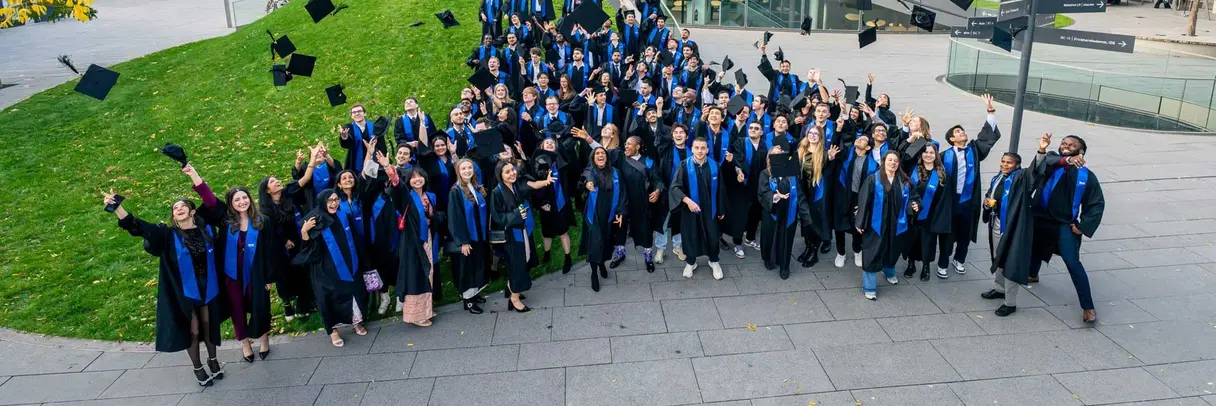 [Translate to German:] a group of students after graduation throwing their hats into the air