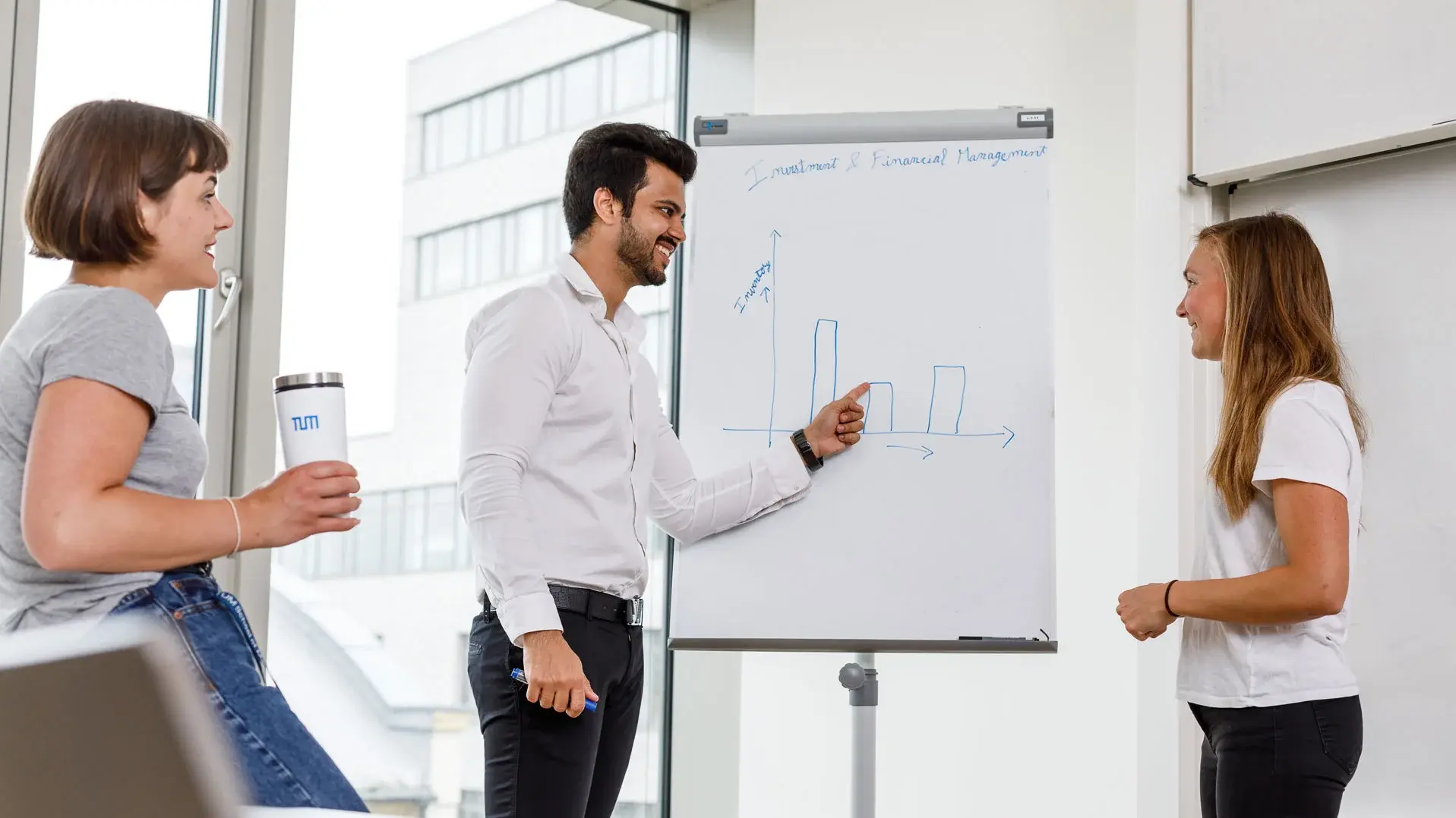 [Translate to German:] Three students working on a flipchart