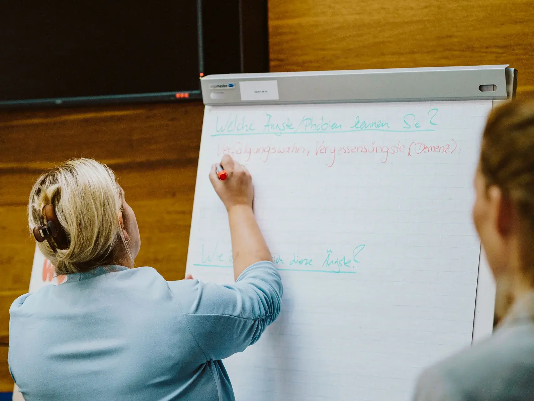 [Translate to German:] Woman writing on flipchart