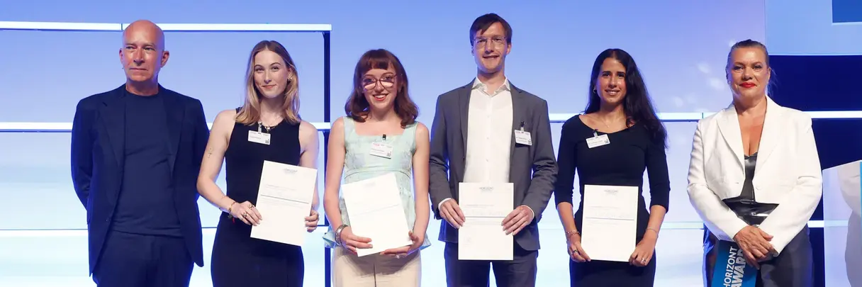 [Translate to German:] A group of women and men in formal clothes standing in a line, holding certificates