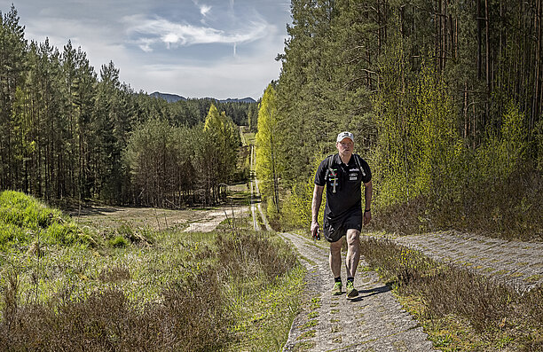 Joey Kelly hiking up a steep path in a forested landscape.