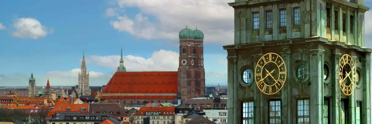 [Translate to German:] Ach church with two bell towers in the background, a green tower with a golden clock in the front