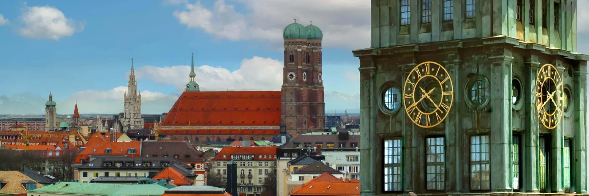 an oldfashioned clock tower in the front, the Munich skyline with the church in the background