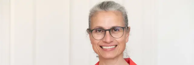 [Translate to German:] Woman in a red blazer and with rimmed glasses