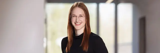 [Translate to German:] Redhaired woman, black dressed, standing, looking into the camera