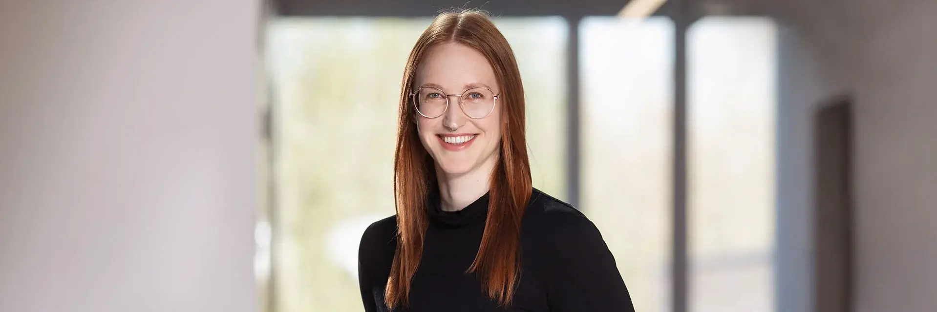 [Translate to German:] Redhaired woman, black dressed, standing, looking into the camera