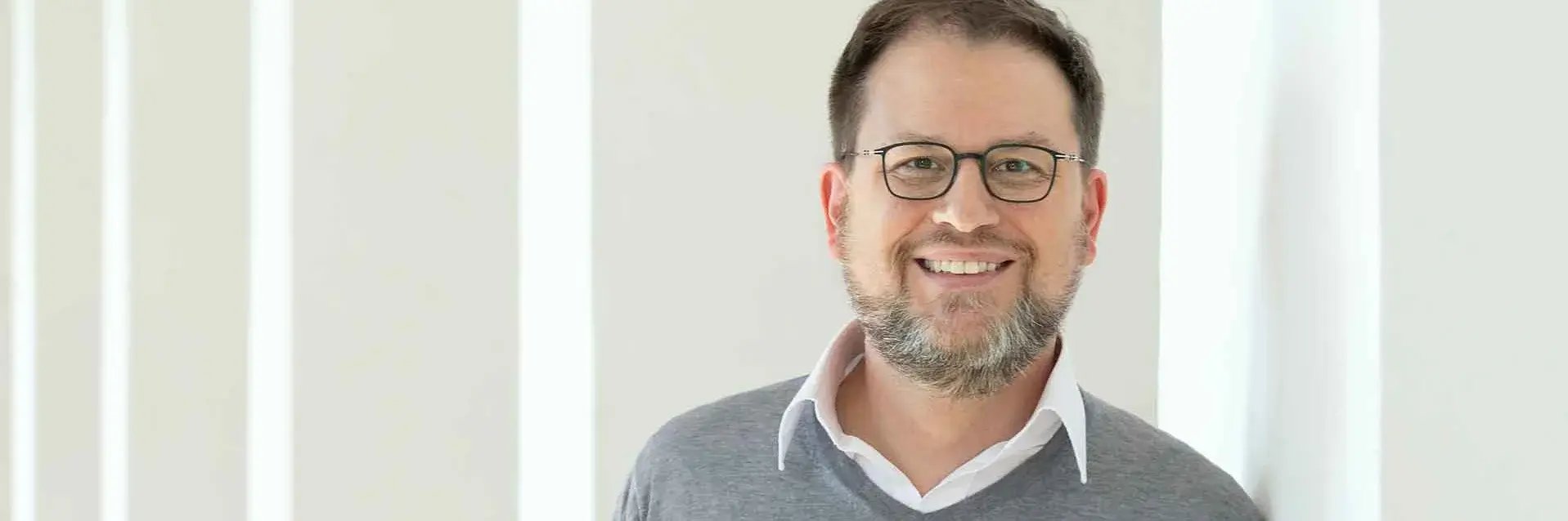 [Translate to German:] Man in gray jumper leaning against a white pillar