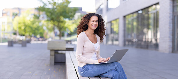 Ein Student arbeitet an einem Laptop draußen auf dem Campus