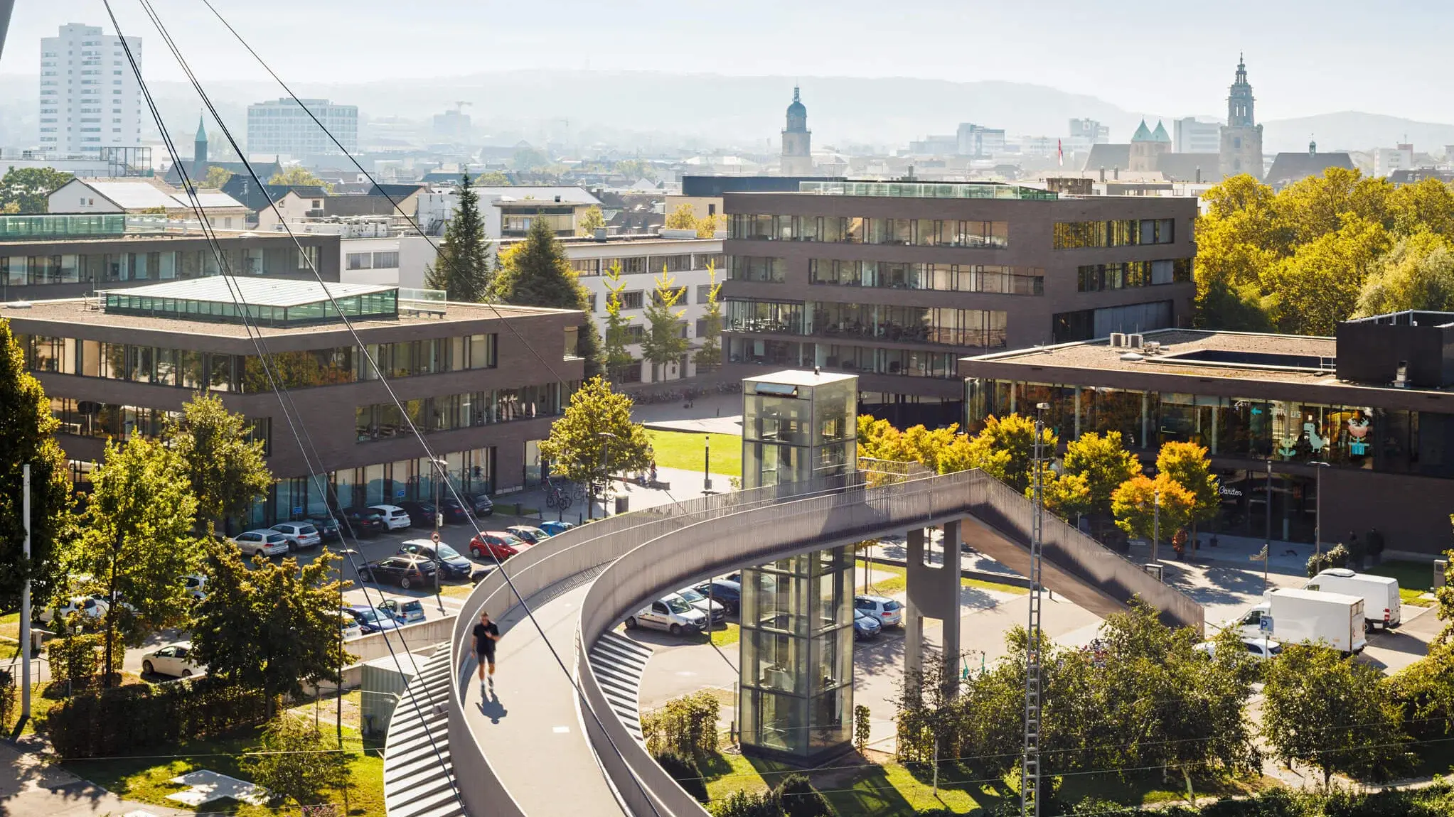 Gebäudekomplex des Bildungscampus Heilbronn mit moderner Fußgängerbrücke, Aufzugsturm und umliegendem Grün.