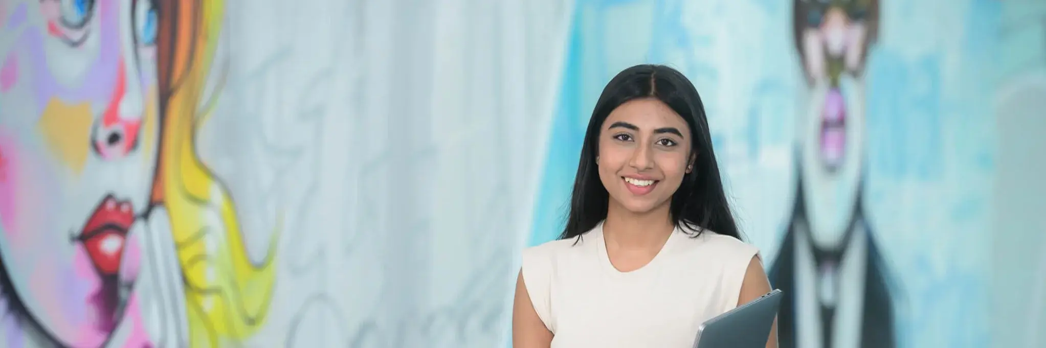 A young woman with a tablet and a young man talking while leaning against a pole