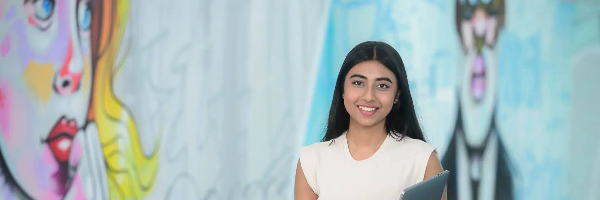 Eine junge Frau mit einem Tablet und ein junger Mann unterhalten sich, während sie sich an einen Pfosten lehnen