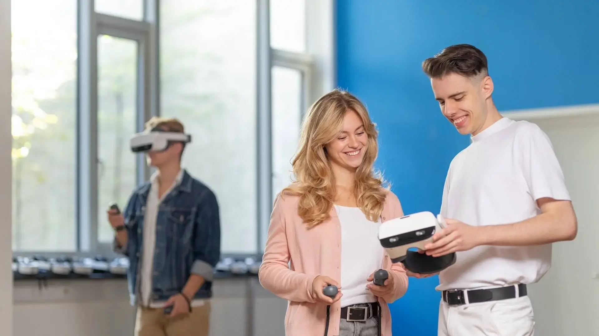 Two students looking at a tablet, and a man using a VR in the background