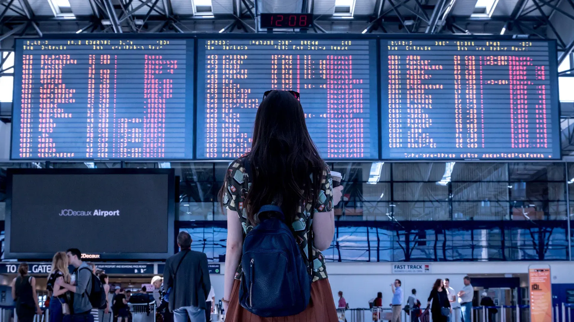 A young woman standing in front of the departure board at an airport